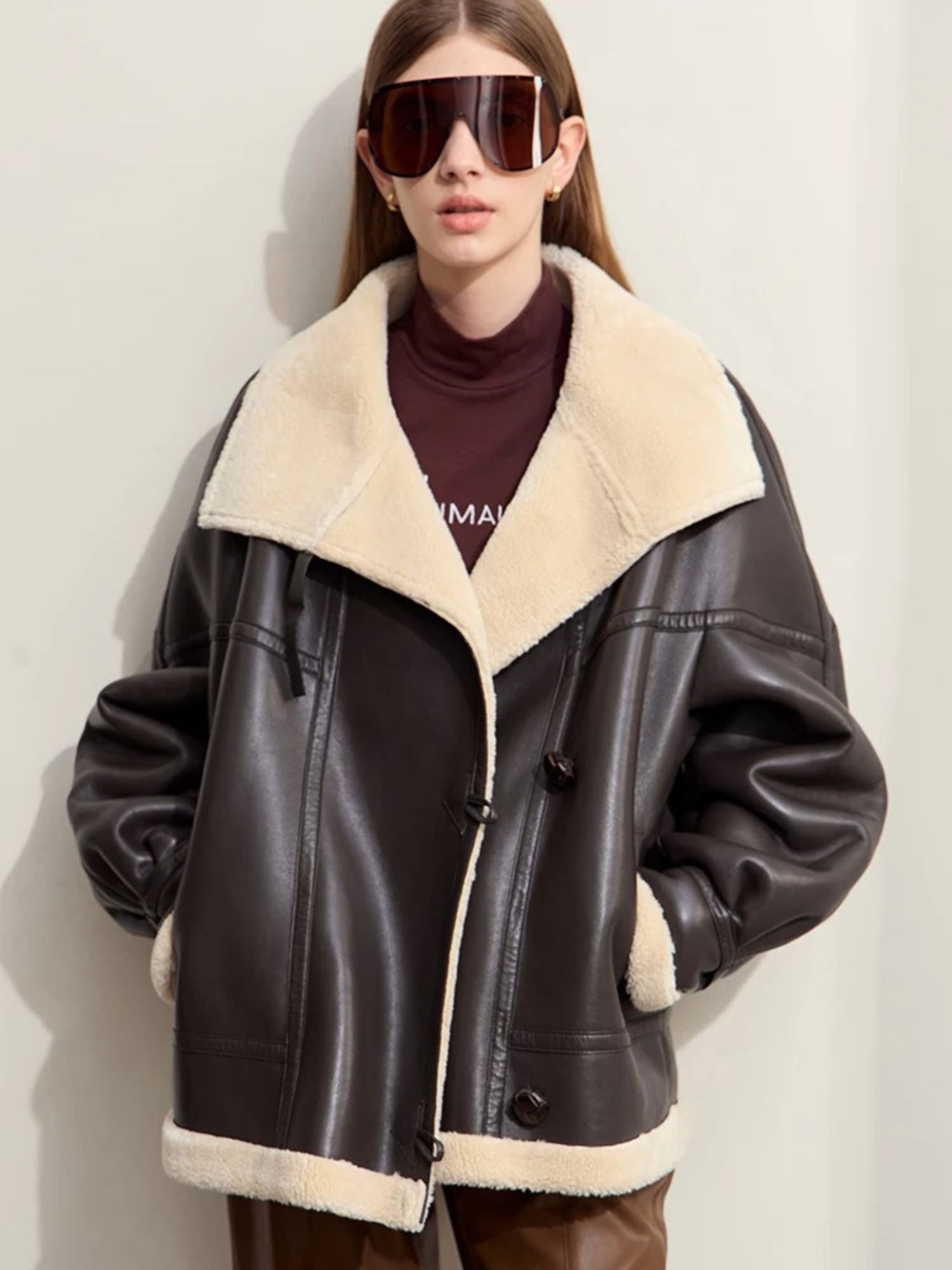 Oversize Fliegerjacke aus braunem Lederimitat mit beigem Shearling-Kragen, Modell mit Sonnenbrille.
