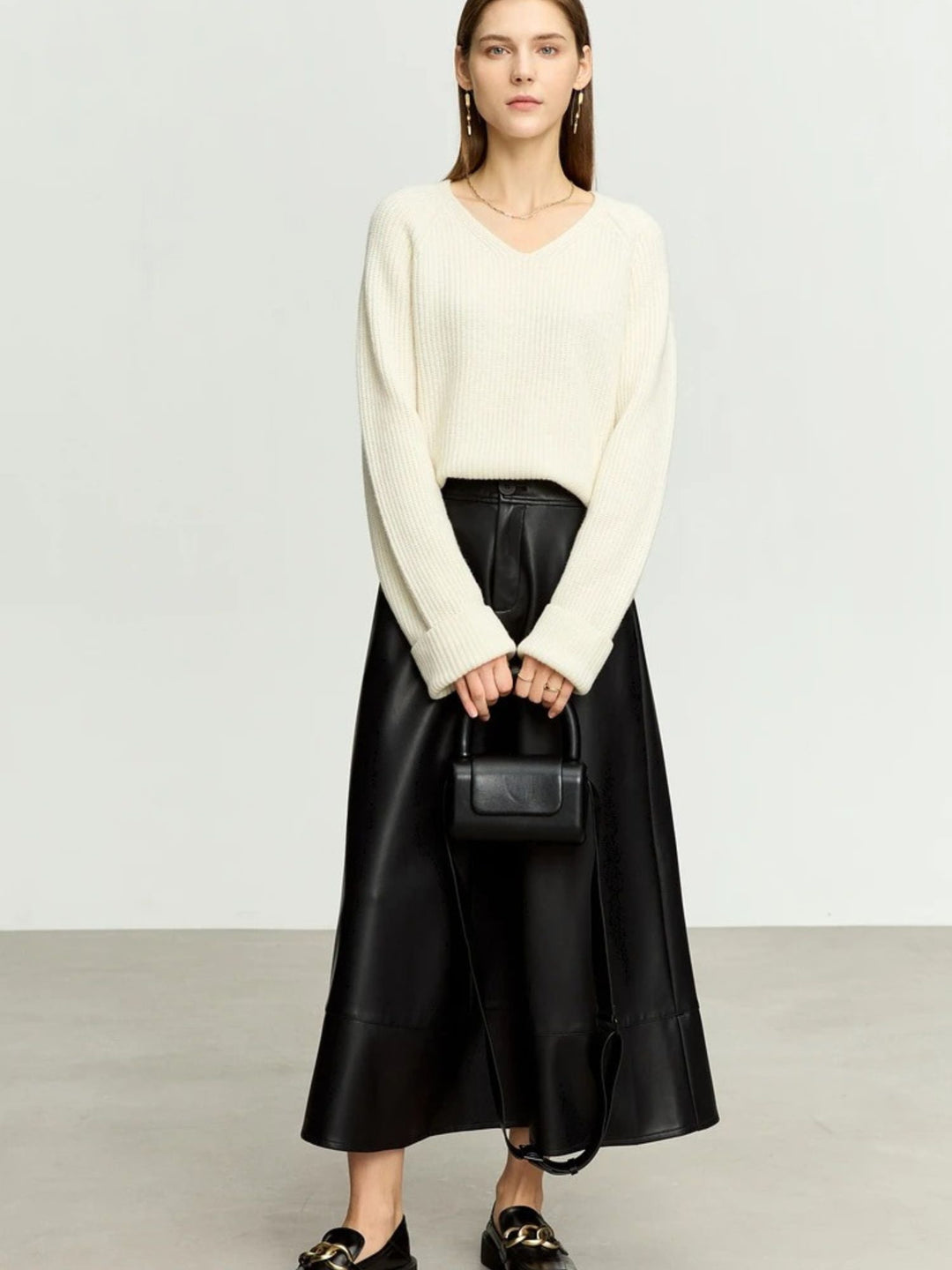 Schwarzer Midirock aus Kunstleder, Modell frontal mit weißem Pullover.

