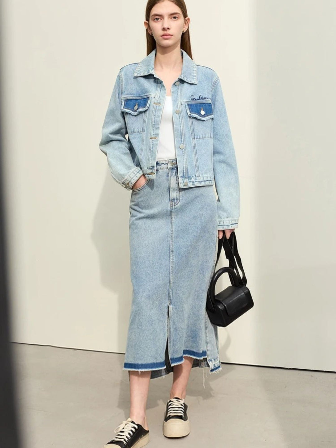 Jeansrock in Midilänge mit Schlitz, kombiniert mit Jeansjacke, Modell frontal.

