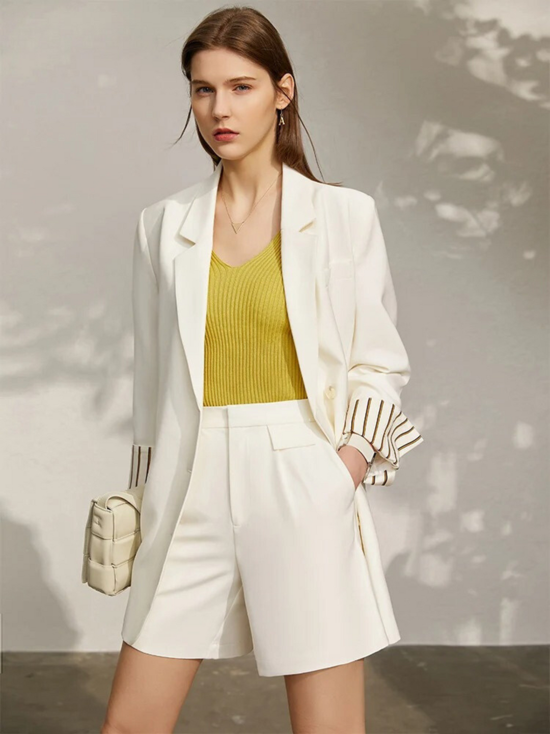 Weißer Damen-Blazer mit Shorts und gelbem Top, Modell frontal mit Tasche.

