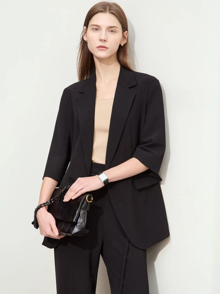 Schwarzer Hosenanzug mit 3/4-Arm-Blazer, Modell frontal mit Clutch.
