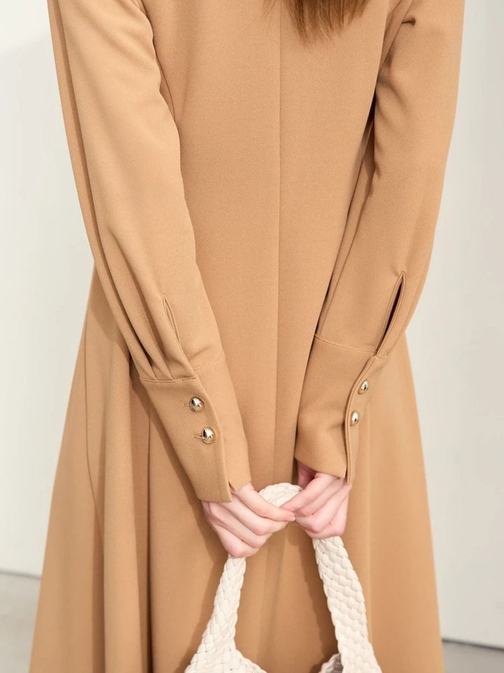 Detailaufnahme: Ärmeldetail mit Goldknöpfen am beigefarbenen Kleid.