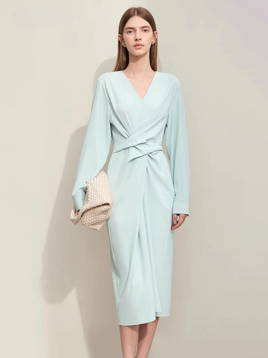 A stylish woman wearing a powder blue, long sleeved, midi dress with a ruching design to cinch the waist,  and a slit at the back for ease of movement. The dress looks lose and comfortable.