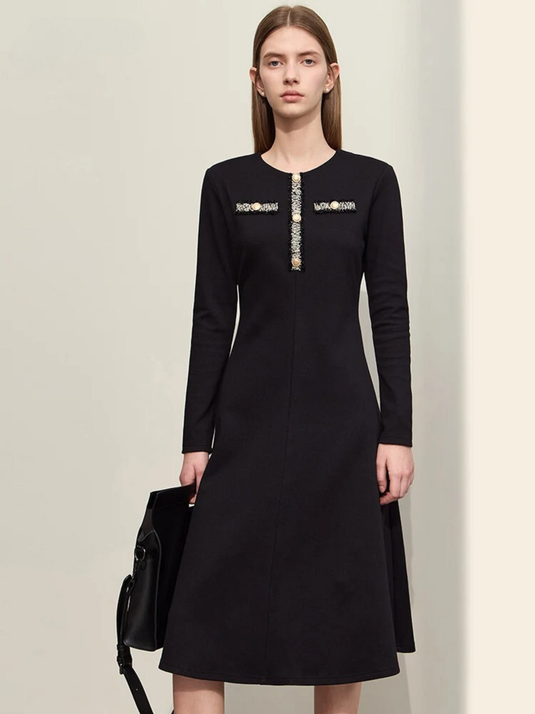 An elegant woman wearing a military inspired dress. The dress has long, fitted sleeves and an a-line silhouette. The bodice showcases a gold embroidery design with buttons. 