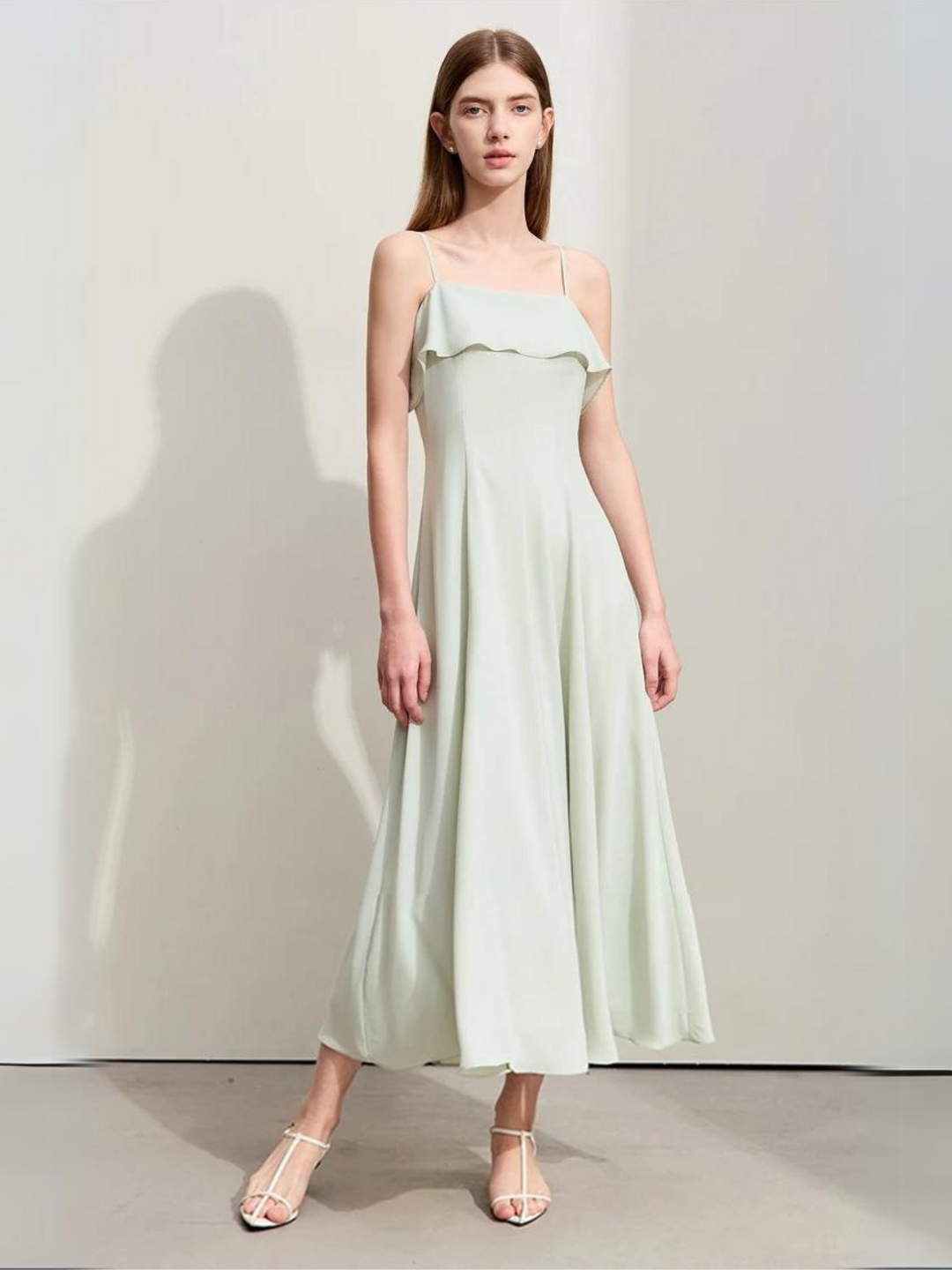 A woman wearing a mint green, simple, angkle-length dress with strappy kitten hills.