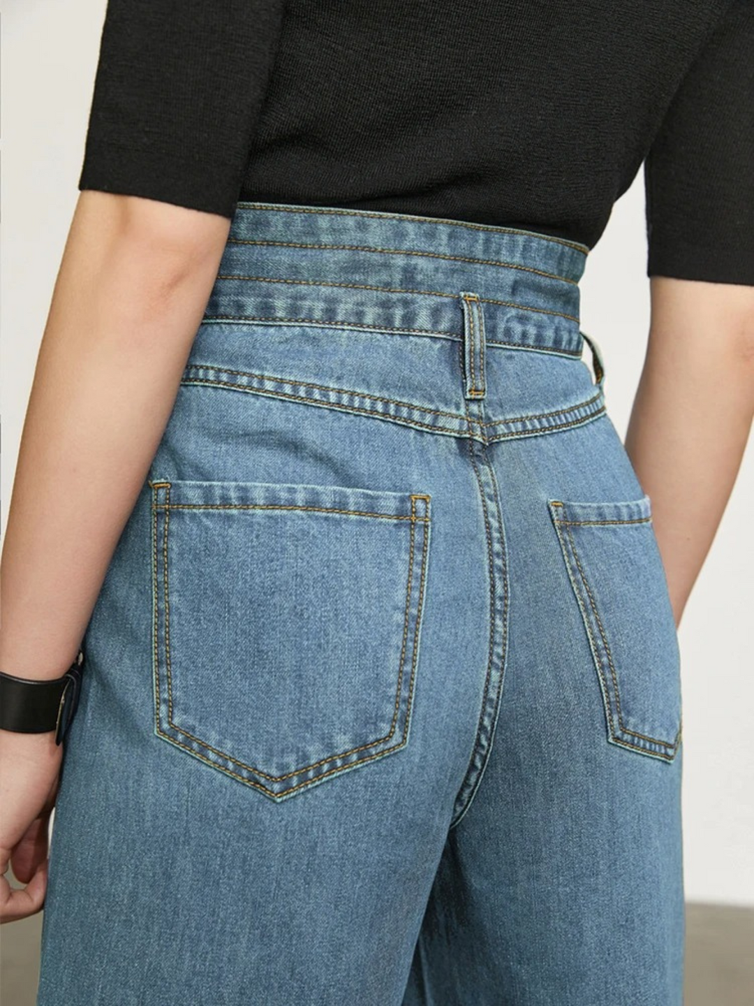 A close up of the backside of a pair of jeans showcasing the cinched waist design and back pockets.